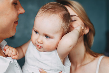 Loving parents hugging and kissing adorable baby daughter. Family, parenting, love and children concept