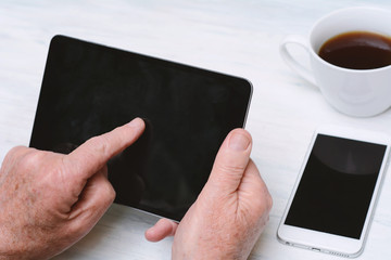Elderly man holding digital tablet with cup of coffee and mobile phone