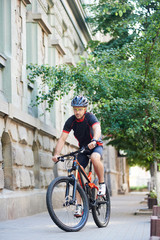 Fototapeta premium Athletic man bicyclist wearing professional cycling clothing and helmet doing extreme sports on bicycle in old city streets. Sportsman training in urban area. Concept of healthy lifestyle