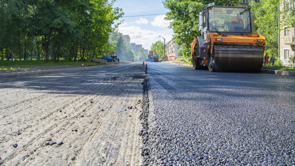 Repair works on laying the asphalt surface on a street road. Steamroller machine for laying asphalt