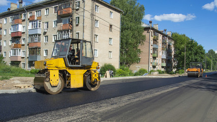 Naklejka na ściany i meble Repair works on laying the asphalt surface on a city street. Steamroller machines for laying asphalt