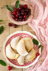 Pies with cherries, sprinkled with powdered sugar and berries of fresh cherries on a wooden surface.