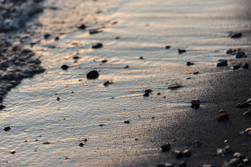 Fototapeta na wymiar A close view of water on a lake shore at sunset, with details of sands and little round stones