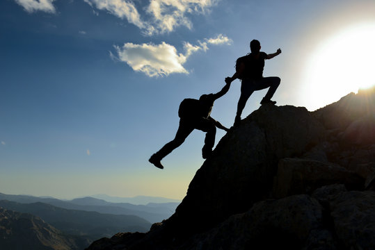 Help and assistance concept. Silhouettes of two people climbing on mountain and helping