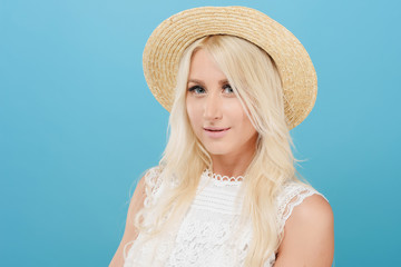 A close-up portrait of a cute blonde girl in a hat on a blue background in the studio. Young model with clean and healthy skin looking at the camera