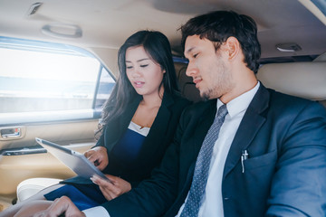 handsome business man and Business woman sitting in luxury limousine car, working on laptop computer, Works anytime and anywhere concept.