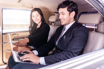 handsome businessman and Business woman sitting in luxury limousine car, working on laptop...