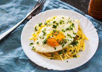 fried egg with Linguine pasta in white plate on wooden table