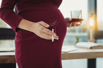 Damaging habit. Young irresponsible woman drinking alcohol and smoking while being pregnant