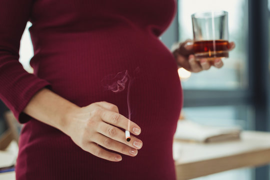 Harmful habit. Young pregnant irresponsible woman having bad habits and smoking while drinking alcohol
