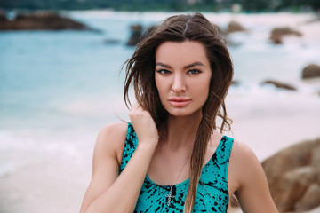A portrait of a dark-haired, suntanned girl in a bright swimsuit, resting on the azure shore, has...