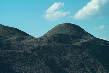 The texture of piles, mountains and hills of fine gravel against the background of the blue sky and clouds Gravel storage limestone mining industry