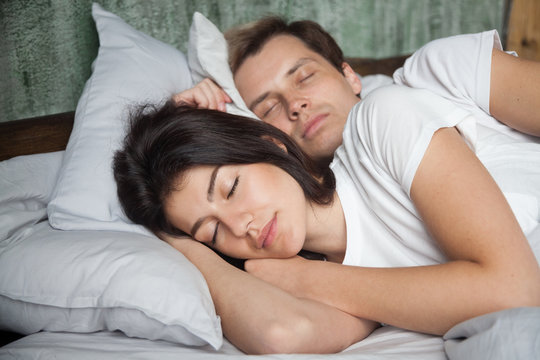 Calm young couple sleeping peacefully together in bed at home, millennial man and woman resting having nap on comfortable soft pillows, beloved spouses being asleep relaxing in cozy bedroom in morning