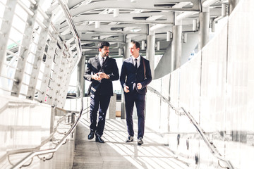 Two smiling businessman coworkers in black suit talking and walking.business people discussing strategy in the modern city