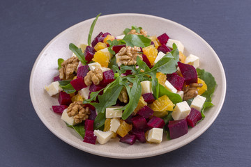 Healthy vegetarian salad with beetroot, green arugula, orange, feta cheese and walnuts on plate
