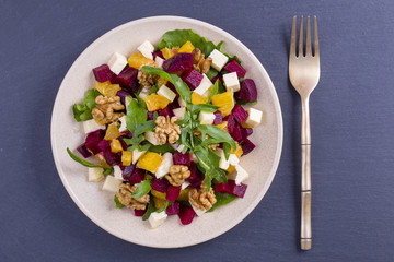 Healthy vegetarian salad with beetroot, green arugula, orange, feta cheese and walnuts on plate, top view