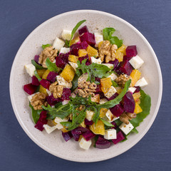Healthy vegetarian salad with beetroot, green arugula, orange, feta cheese and walnuts on plate, top view