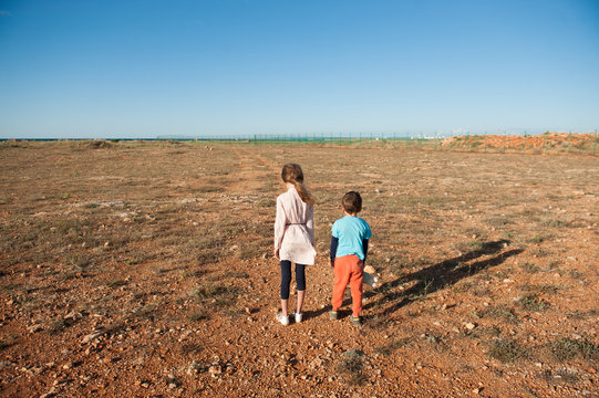 two sad children refugees walking holding hands in hot desert in summer