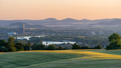 Panorama of the beautiful sunset in western Germany, a field of wheat, in the distance a flowing river, railway bridge and chimney of a nuclear power plant.