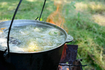 Fish soup boils in cauldron at the stake on the nature. Soup in a pot in the fire.  Close-up.