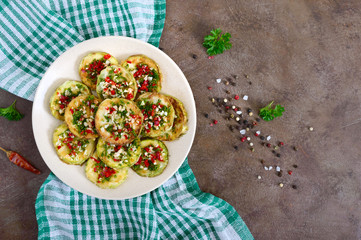 Fried circles of young zucchini with garlic, red pepper, greens on a plate. Vegetarian menu. Top view.
