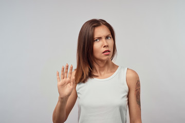 Body language. Stressed out woman wearing her blonde hair loose posing against gray studio wall, keeping hands in stop gesture, trying to defend herself as if saying: Stop that, Stay away from me