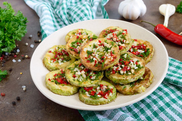 Fried circles of young zucchini with garlic, red pepper, greens on a plate. Vegetarian menu. Close up