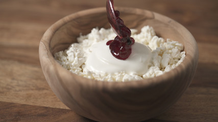 closeup adding cowberry jam to cottage cheese in wood bowl