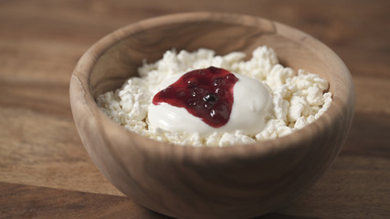 closeup adding cowberry jam to cottage cheese in wood bowl