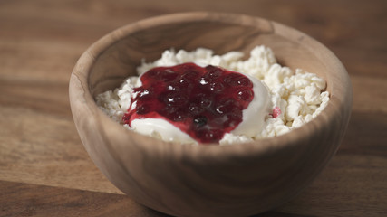 closeup adding cowberry jam to cottage cheese in wood bowl