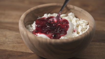 closeup adding cowberry jam to cottage cheese in wood bowl