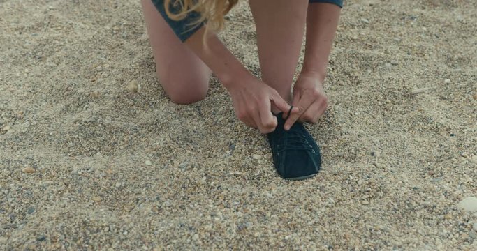 Young woman tying her running shoes on the beach
