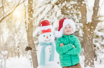 portrait of smiling boy in red christmas hat with snowman on background. Space for text
