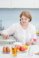 Obraz na płótnie Canvas senior woman pours milk for breakfast in the kitchen