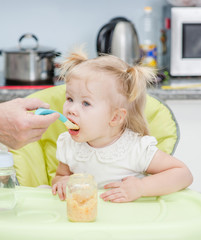 Parent  feeding hungry baby with spoon at kitchen
