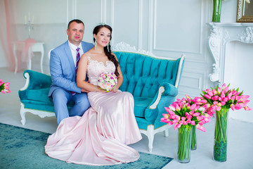 Lovely wedding couple sitting together on sofa in luxurious white room