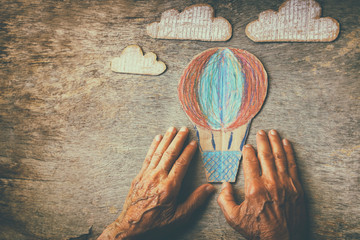 A close up of an elderly man holding a paper air baloon on a wooden table. Concept of thinking about childhood dreams, sadness and loneliness.