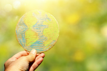 man hand holding earth globe in front of outdoor green bokeh background.