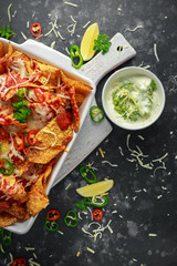 Maxican-style tortilla nachos chips topped with tomato salsa, sliced chilies and melted cheese served with lemon wedges and avocado yogurt dip