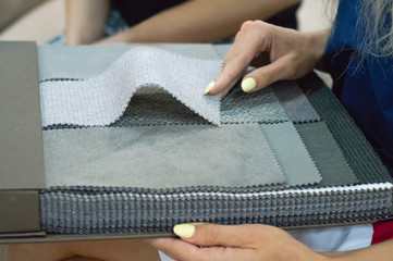 The girl is viewing samples of fabric for furniture in home or commercial building. Large color catalog of fabric. Design. 