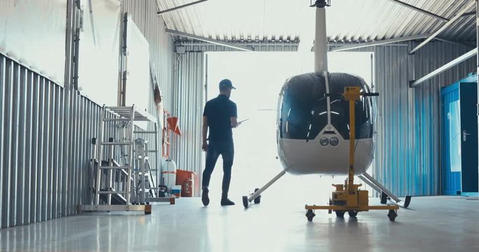 Male mechanic in uniform examining helicopter. Pre flight inspection at the airport. 4K UHD