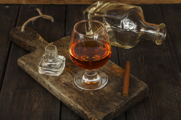 A glass of cognac or whiskey with a cigar on a wooden old table. Whiskey cognac in a glass.