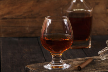A glass of cognac or whiskey with a cigar on a wooden old table. Whiskey cognac in a glass.