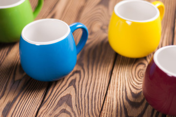 Four colored empty ceramic clean mugs on old worn brown wooden table