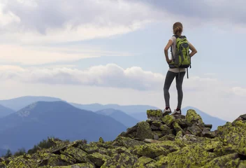 Foto op Canvas Back view of young slim girl with backpacks standing on rocky mountain top against bright blue morning sky enjoying foggy mountain range panorama. Tourism, traveling and healthy lifestyle concept. © bilanol