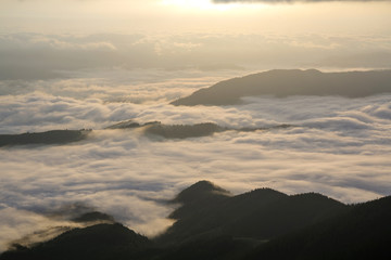 Fantastic view of mountain valley covered with low white puffy like snow clouds stretching to foggy...