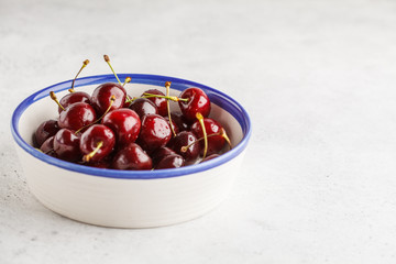 Ripe red cherry in a white bowl on a light background, copy space. Healthy clean eating concept