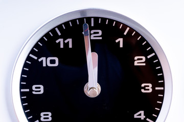 Closeup of modern black chrome clock on white background indicates twelve o'clock, wake up, time for action, time up or midday. Time passing concept for business urgency and running out of time.