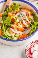 Bright vegan salad with arugula, sweet potato, radish, tahini dressing and cucumber, white background. Healthy vegan food concept.