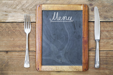 Blackboard menu with fork and knife on wooden background, free copy space